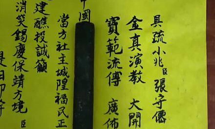 一張黃色紙張上書寫的疏文，使用傳統漢字，疏文中提到‘金真演教’、‘寶篆流傳’等文字，旁邊擺放一支墨條。