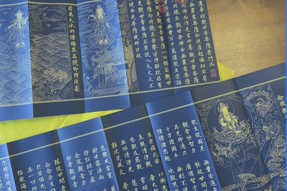 多張藍底金字的佛教經文，經文中繪有觀世音菩薩的圖像，經文排列整齊，呈現莊嚴的佛教氛圍。